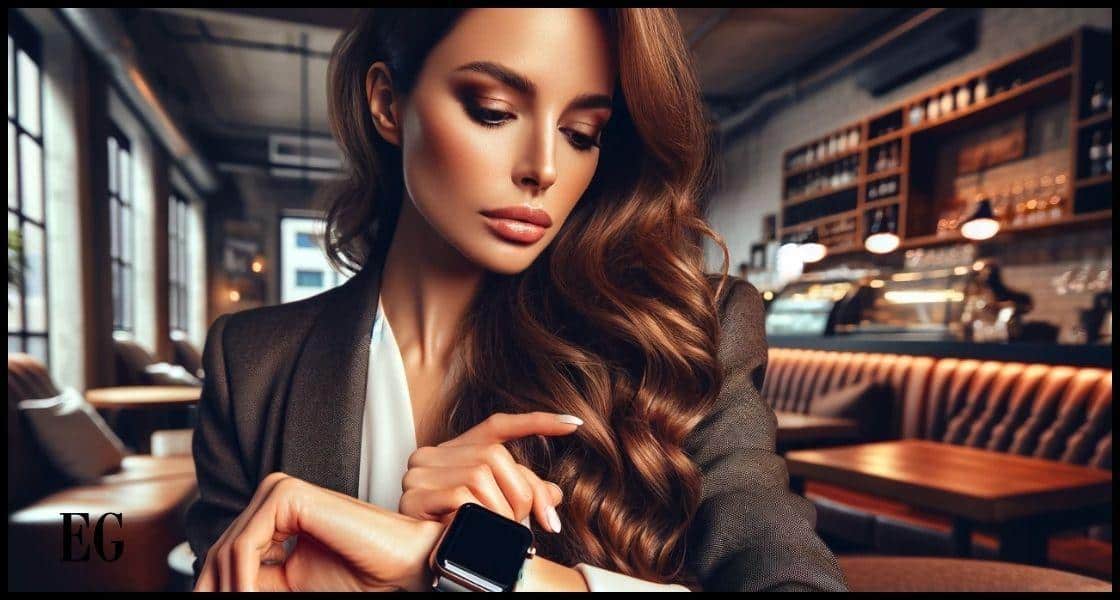 mujer de origen hispano, en sus primeros años treinta, con cabello castaño ondulado y largo. Está vestida con un atuendo elegante y casual de negocios, y mira su reloj inteligente con una expresión reflexiva. El reloj luce sofisticado y de alta tecnología. El fondo revela el interior acogedor de una cafetería urbana, con iluminación suave, asientos cómodos y un ambiente relajado, transmitiendo una sensación de estilo de vida moderno e integración tecnológica
