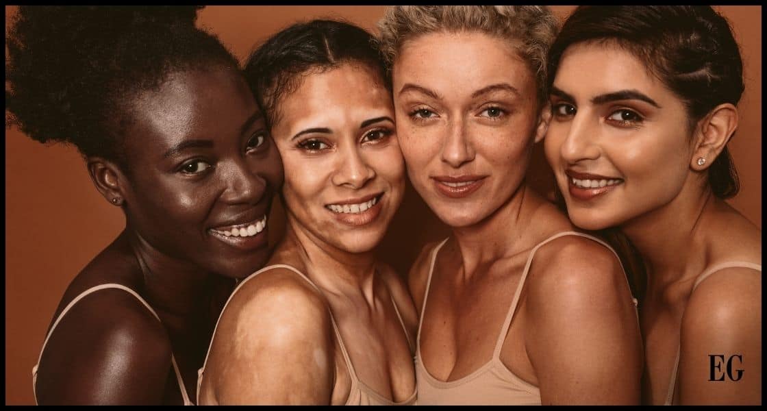 Cuatro mujeres de diferentes etnias y tipos de piel sonriendo y posando juntas para una fotografía. Todas parecen llevar tops sin mangas y tienen el cabello recogido o apartado de la cara, destacando su belleza natural y diversidad.
